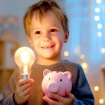 Kind hält Glühbirne und Sparschwein in gemütlichem Raum